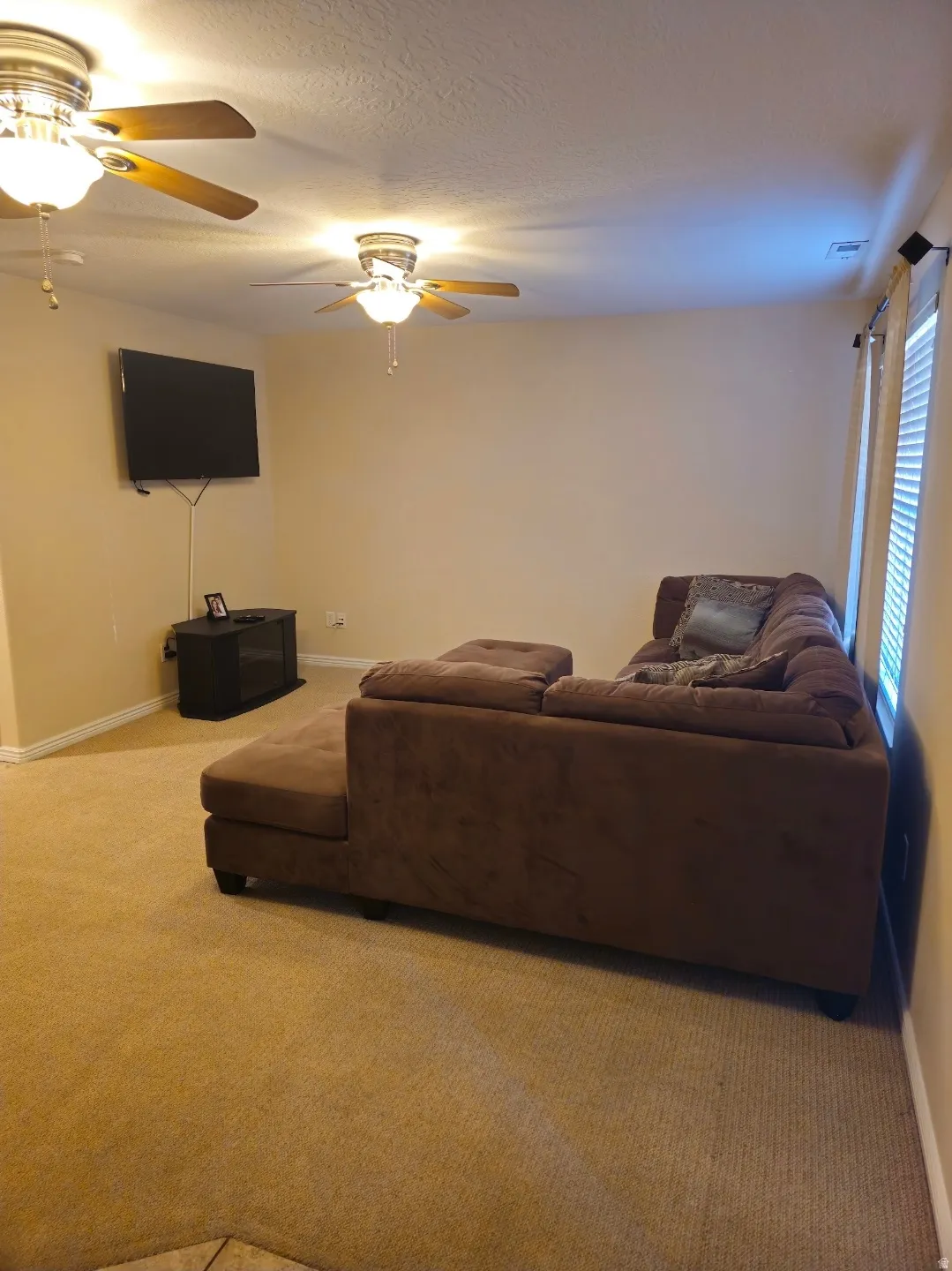 Carpeted living area featuring two ceiling fans with integrated lighting
