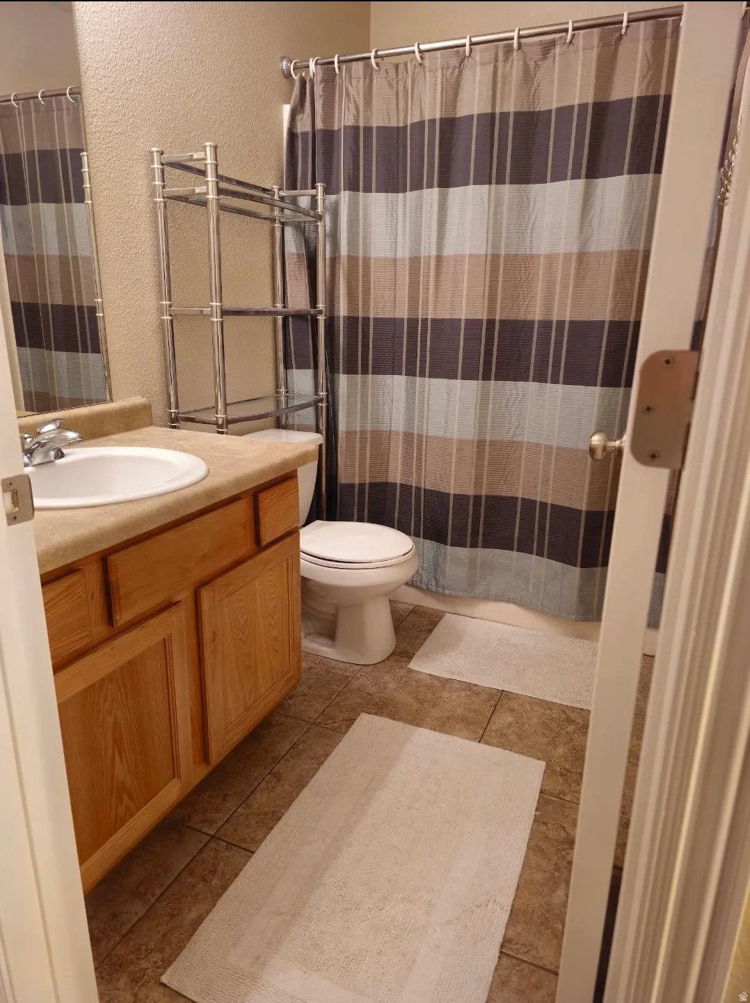 Full bathroom featuring a wood-finish vanity with an integrated sink, a neutral-toned countertop, and tile flooring