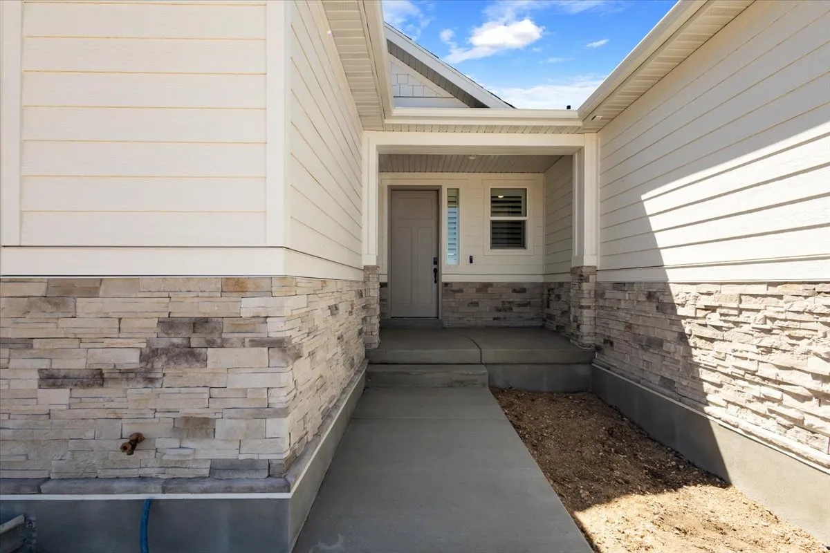 Exterior entry featuring a covered porch, light-toned stone veneer, horizontal siding, and a concrete walkway