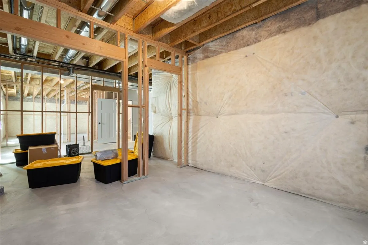 Unfinished basement featuring exposed wood framing, concrete flooring, and insulated perimeter walls