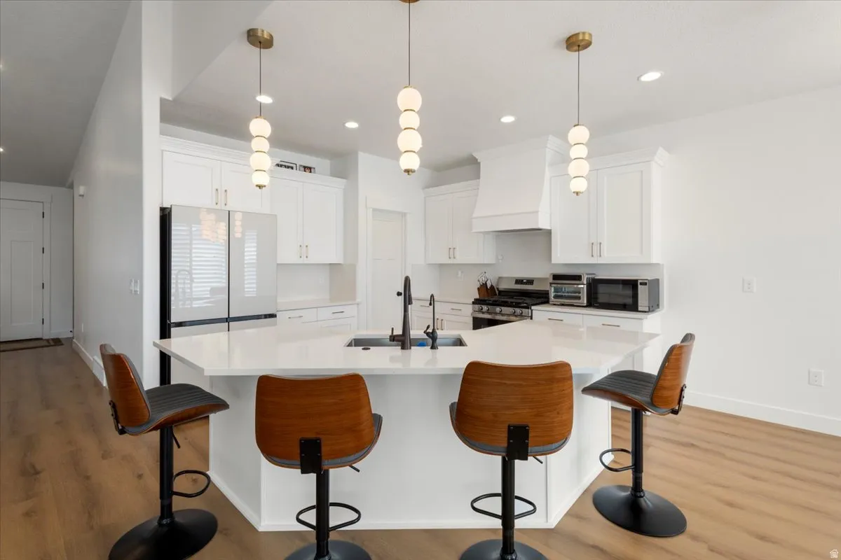 Modern kitchen featuring a large central island with seating, white shaker cabinetry, stainless steel appliances, and wood-finish flooring