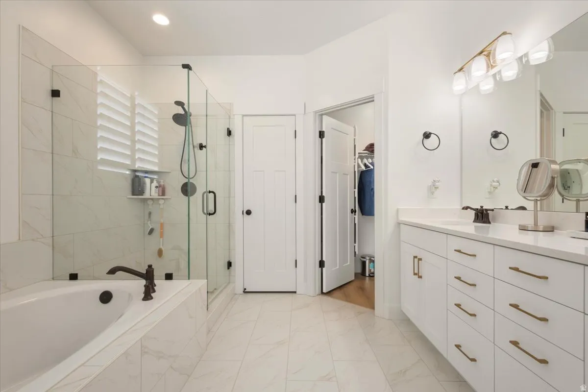 Spacious bathroom featuring a double vanity with white cabinetry and brass hardware, a walk-in shower with clear glass enclosure, a built-in soaking tub, and tile flooring