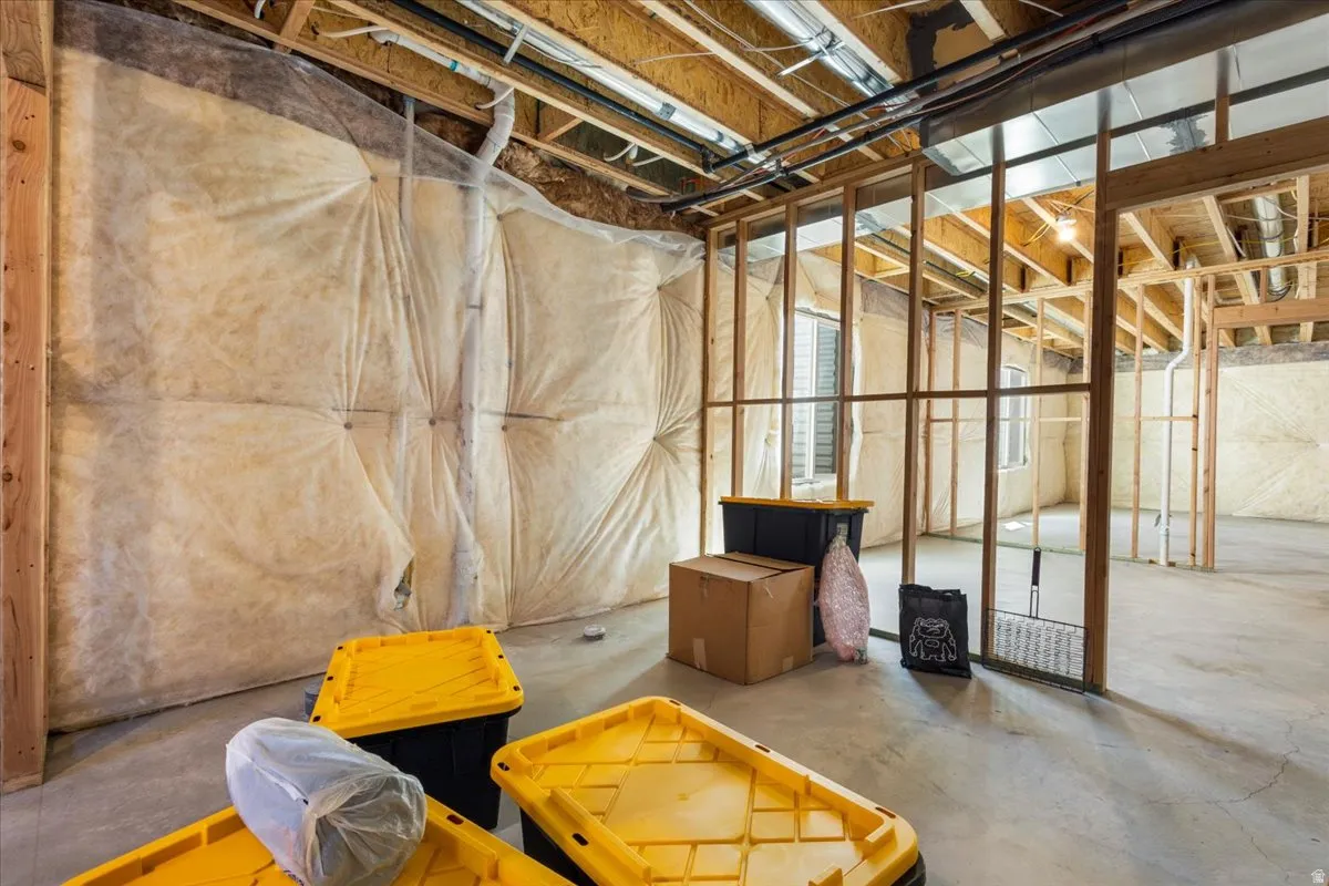 Unfinished basement featuring exposed wood framing, concrete flooring, insulated walls, visible ceiling joists, and a window