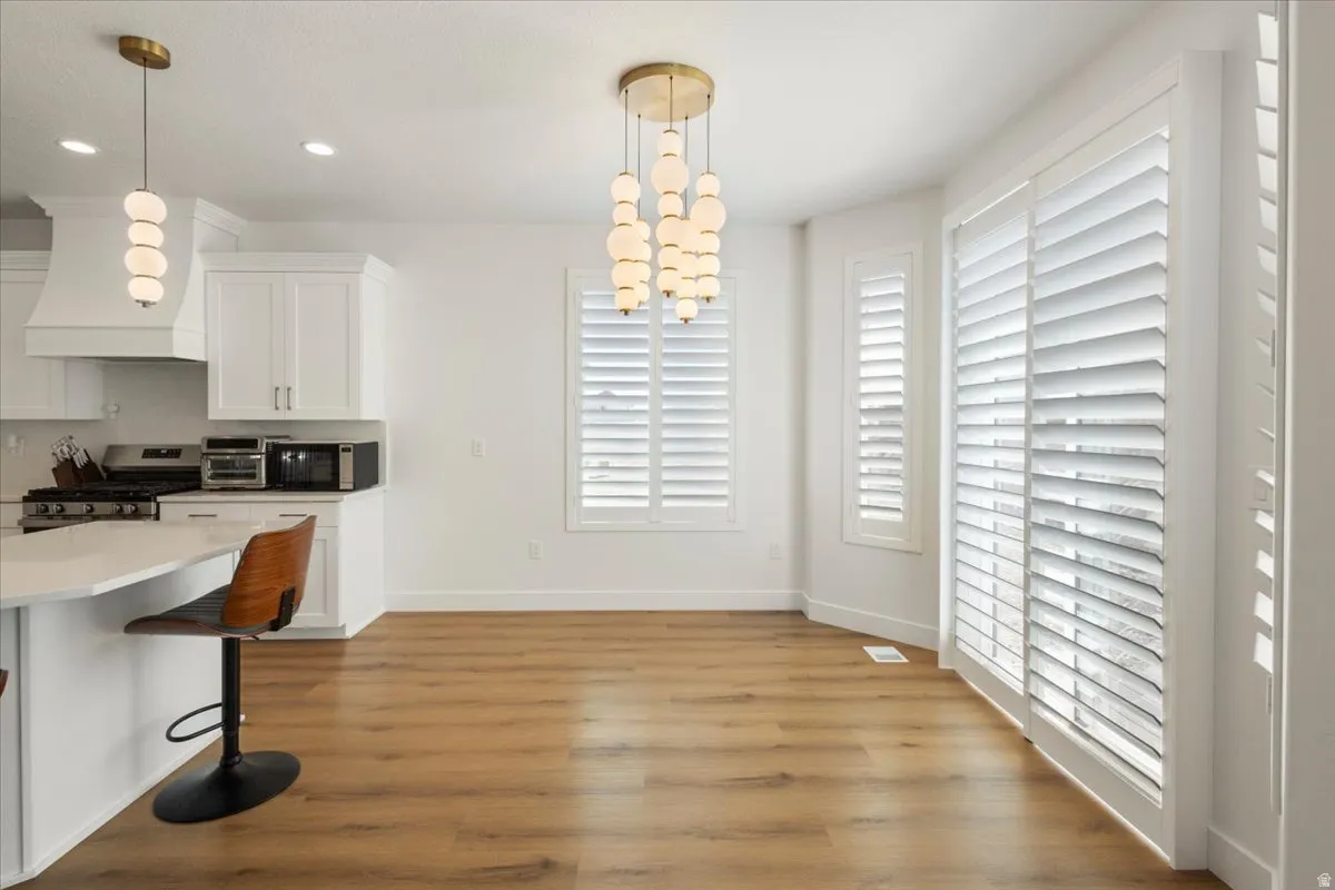 Open-concept living space with wood-finish flooring, white cabinetry, a kitchen island with a light-colored countertop, and a contemporary multi-bulb chandelier