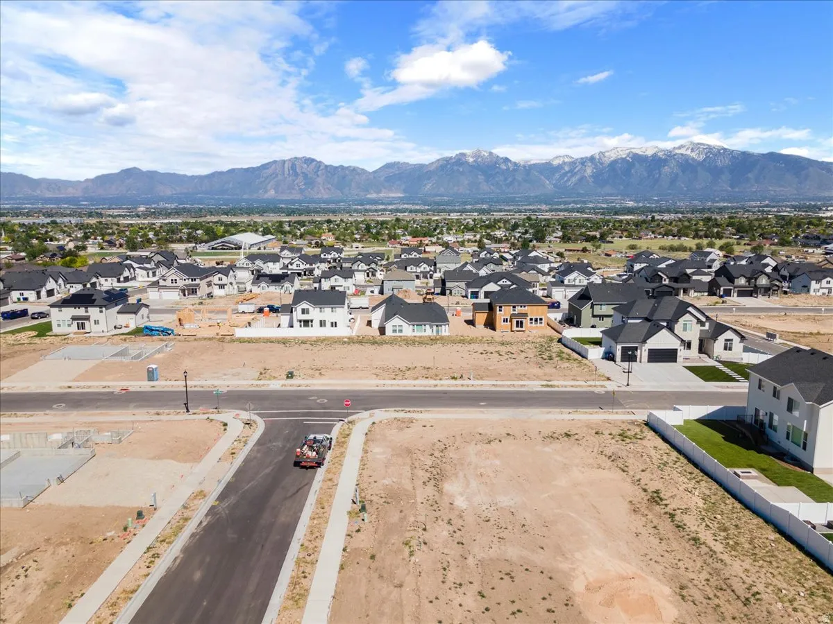 Expansive building lot situated within a developing neighborhood, featuring paved streets, concrete sidewalks, and a mountainous backdrop