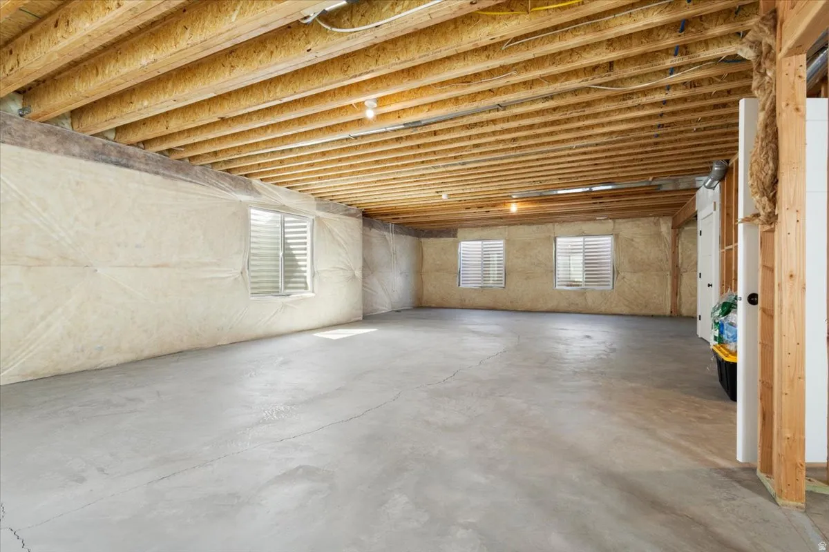 Expansive unfinished basement featuring a concrete floor, exposed wood ceiling joists, and multiple windows