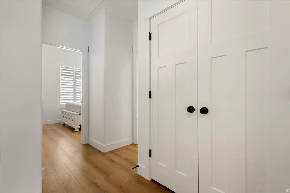Hallway featuring wood-finish flooring, white paneled doors with black hardware, and a white baseboard trim