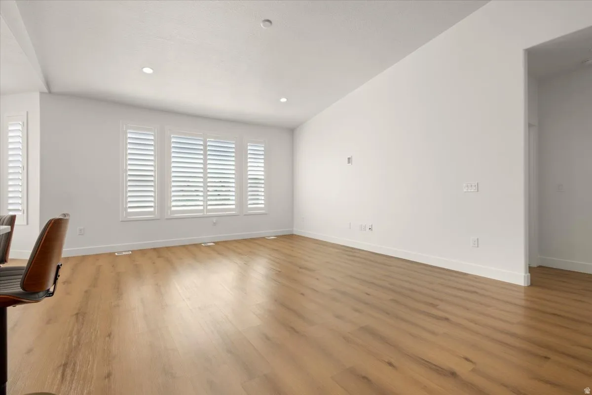 Spacious room featuring wood-finish flooring, white baseboards, and multiple windows with plantation shutters