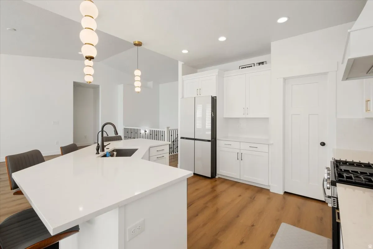 Kitchen featuring a large island with white countertop and integrated sink, white shaker-style cabinetry, stainless steel appliances, and wood-finish flooring