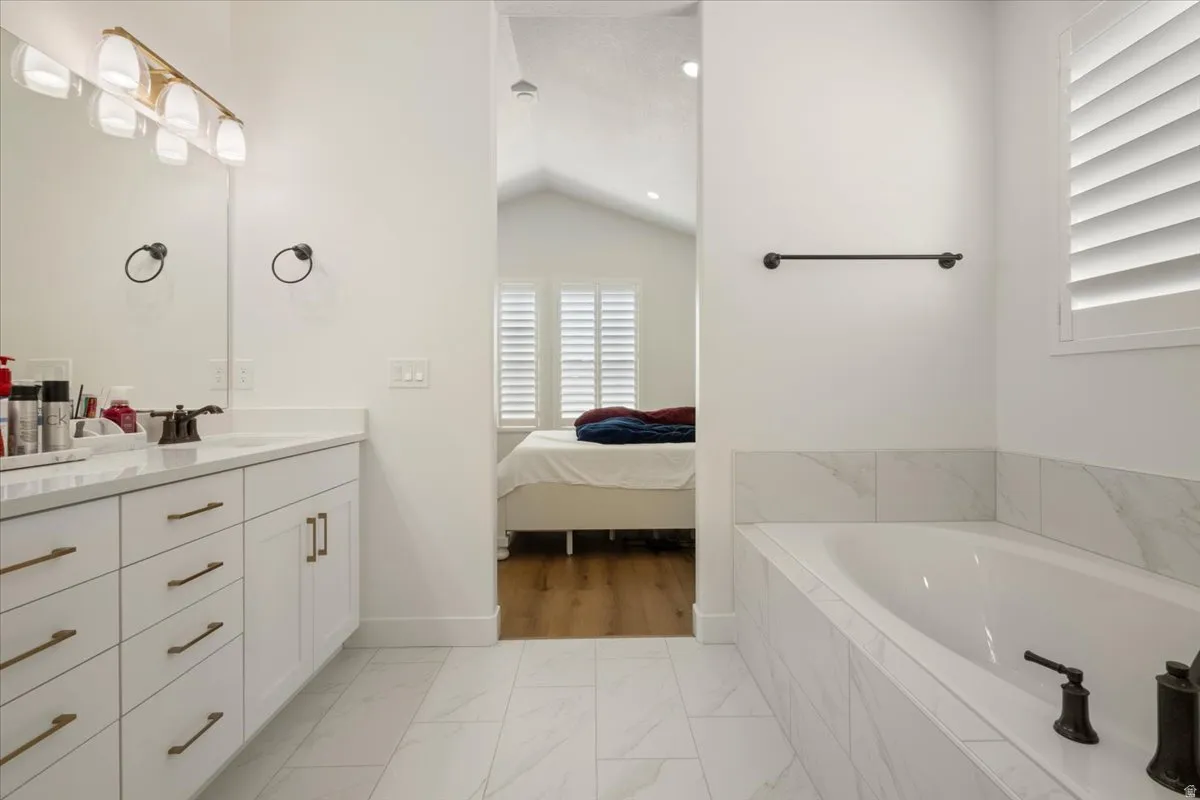 White tiled bathroom featuring a built-in bathtub with a dark bronze faucet, a double vanity with white cabinetry and bronze hardware, and a large mirror
