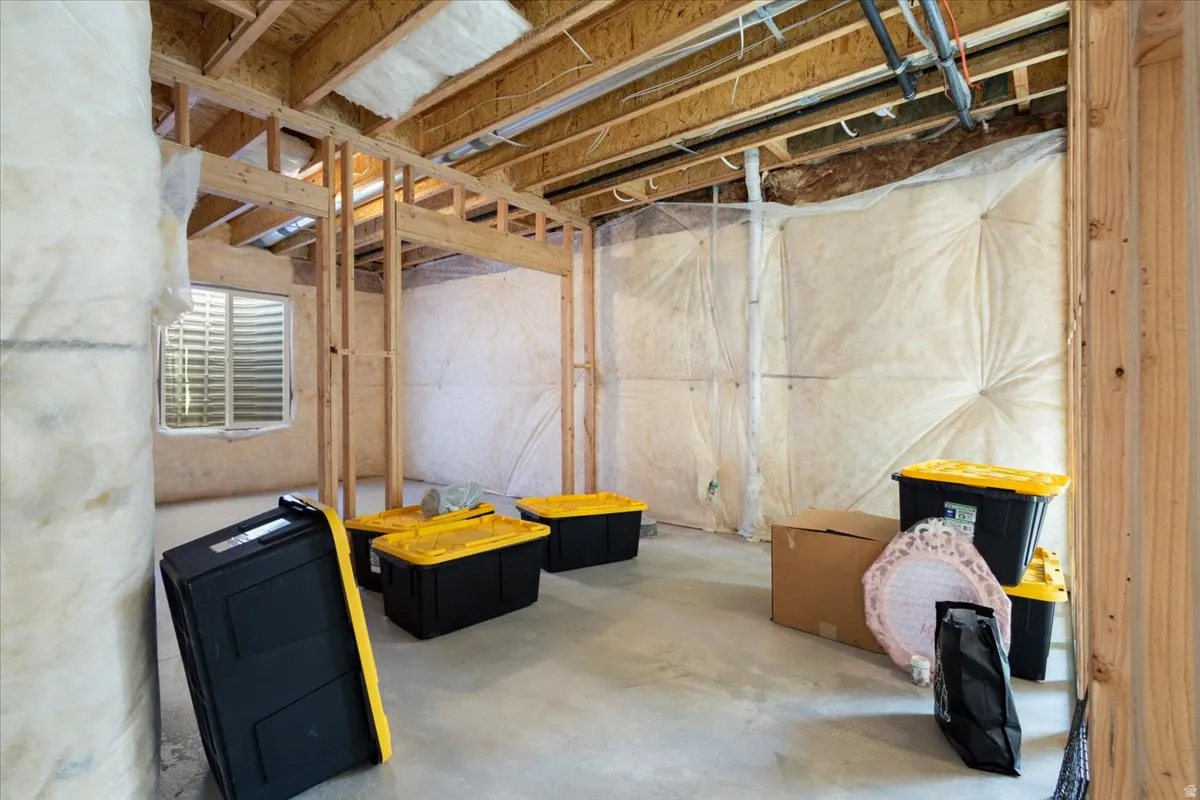 Unfinished basement presenting framed walls, exposed ceiling joists, insulation, and a ground-level window with louvered blinds