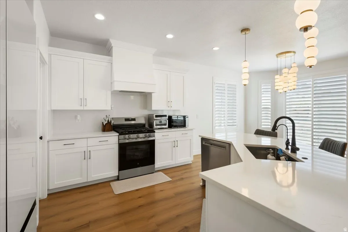 Contemporary kitchen featuring white shaker cabinetry, stainless steel appliances, light wood-finish flooring, and crisp white countertops
