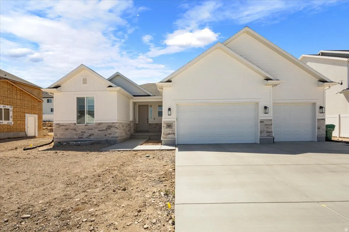 Contemporary ranch-style exterior featuring a light-toned facade with stone accents, a prominent front entry, a two-car garage, and a concrete driveway