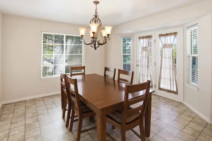 Dining area featuring tiled flooring, a multi-light chandelier, a large window with blinds, and French doors flanked by additional windows