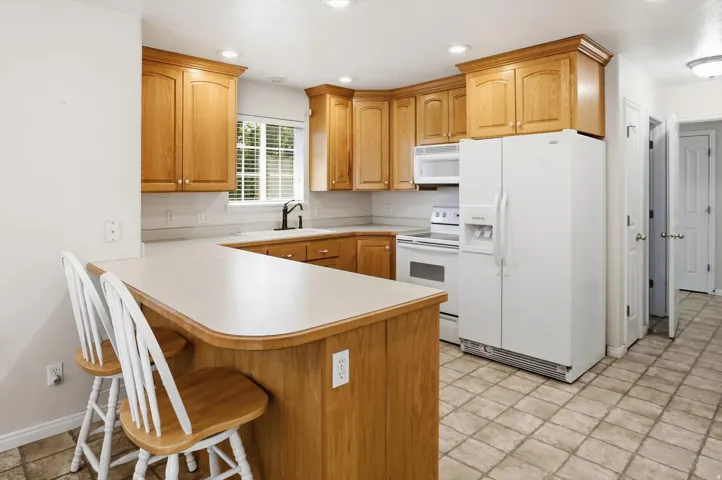 Kitchen featuring light wood cabinetry, light-toned countertops, integrated white appliances, a peninsula with bar seating, and recessed lighting