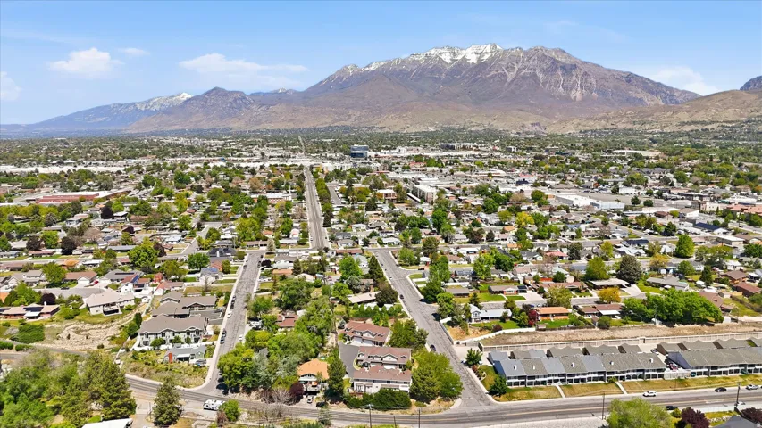 Expansive aerial of a residential area with varied housing styles, mature trees, and a clear mountain backdrop featuring snow-capped peaks