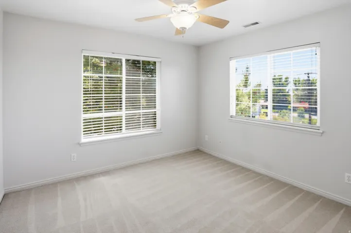 Bright room featuring two windows with white blinds, light gray wall paint, and neutral carpeting