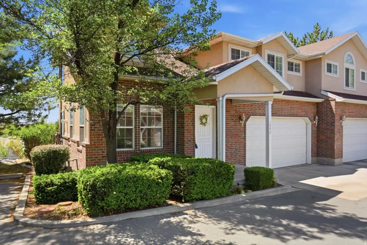 Brick and stucco exterior featuring multiple windows, a white front entry door, an attached garage with a white garage door, and mature landscaping