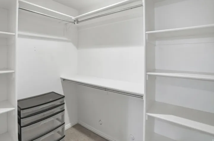 Walk-in closet featuring built-in shelving, multiple hanging rods, and neutral carpet flooring