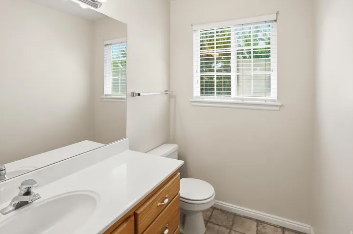 Bathroom featuring a wood-finish vanity with a white countertop and integrated sink, a large wall mirror, and a window with horizontal blinds