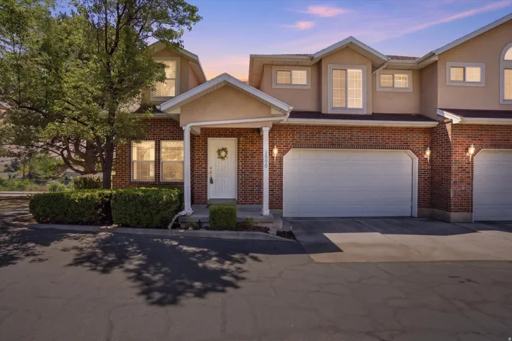 Brick and stucco townhome exterior featuring an attached two-car garage, covered entry, and mature landscaping