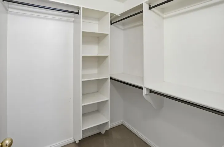 Walk-in closet featuring white built-in shelving, multiple hanging rods, and carpet flooring