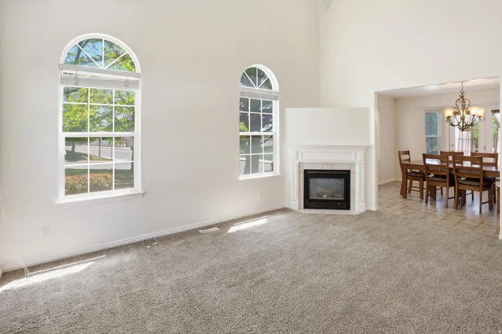Bright living space featuring a corner fireplace with a white mantel, arched windows, and soft carpet flooring
