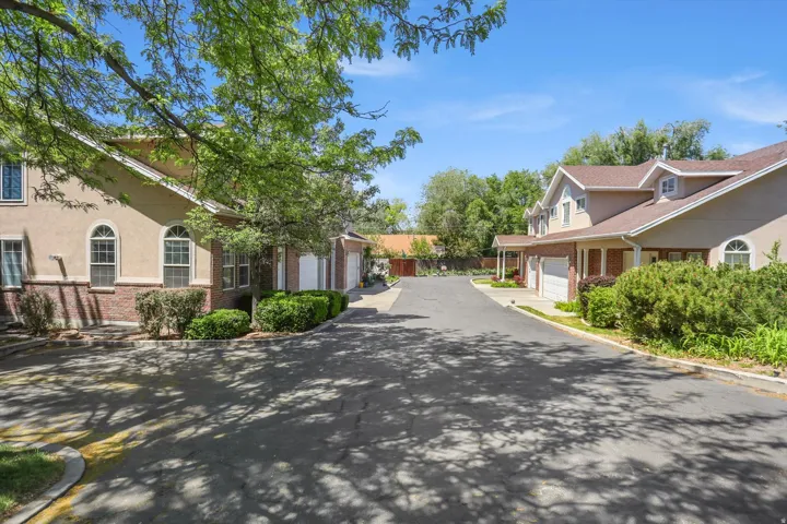 Private drive with multiple stucco and brick residences featuring arched windows, attached garages, and mature landscaping