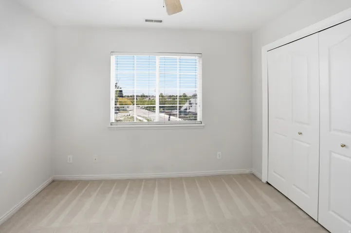 Neutral-toned room featuring a large window with horizontal blinds, light beige carpet, and bi-fold closet doors