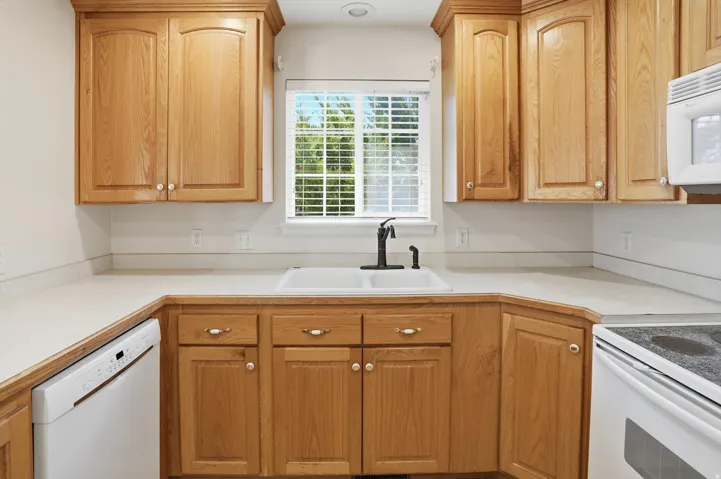 Kitchen featuring light wood cabinetry, white countertops, a double basin sink with a matte black faucet, a built-in dishwasher, and a window with blinds