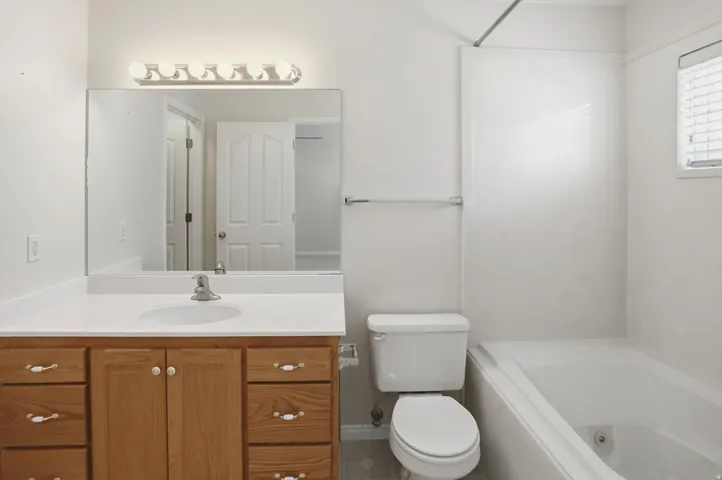 Bathroom featuring a light wood-finish vanity with a white countertop and integrated sink, a large wall-mounted mirror, and a five-bulb vanity light fixture