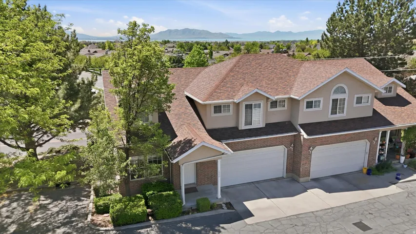 Two-story property featuring a brick and stucco facade, dual attached two-car garages, a prominent arched window on the upper level, and a brown shingle roof