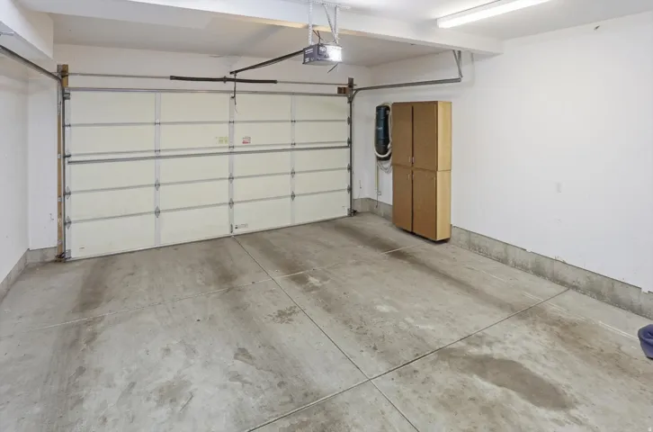 Spacious garage featuring a sectional overhead door, concrete flooring, overhead fluorescent lighting, and built-in storage cabinetry