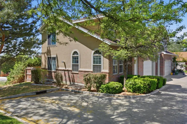 Stucco and brick exterior with arched windows, mature landscaping, and an attached two-car garage