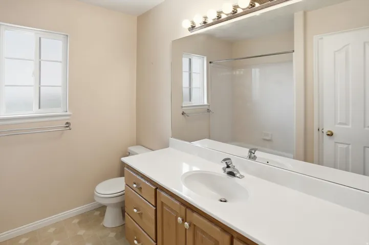 Bathroom featuring a wood-finish vanity with an integrated sink, a large wall-mounted mirror, and overhead vanity lighting