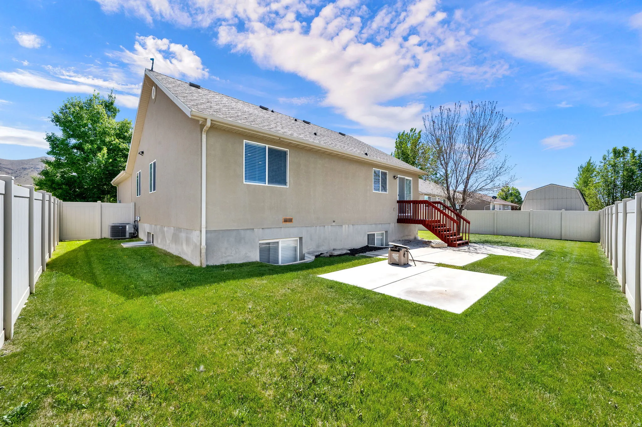 Expansive backyard featuring a manicured lawn, two concrete patio areas, a privacy fence, and a multi-level deck with wood-finish stairs
