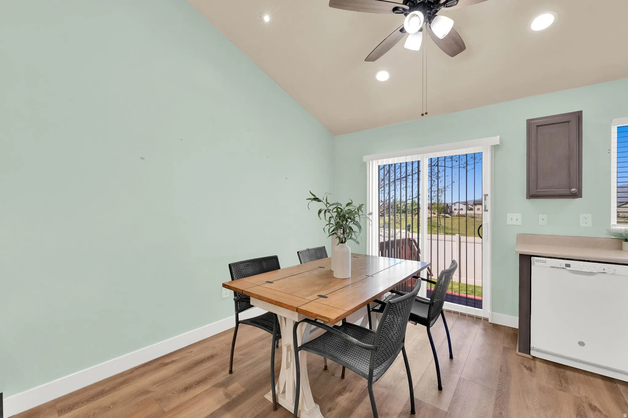 Sliding glass door with security bars, wood-finish flooring, vaulted ceiling with ceiling fan, recessed lighting, and a built-in dishwasher