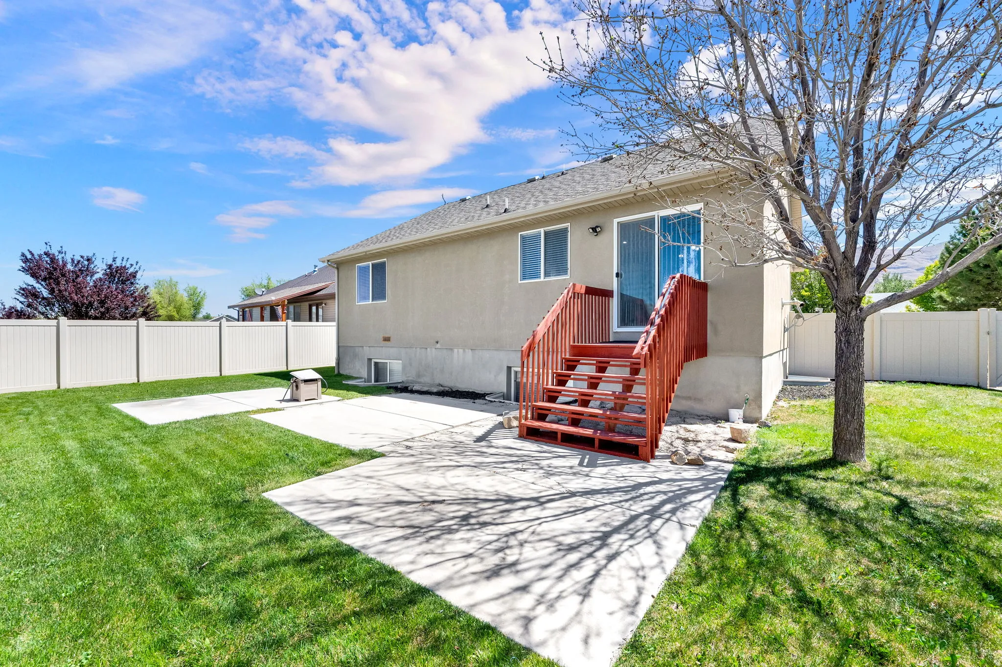 Expansive backyard featuring a manicured lawn, concrete patio areas, a privacy fence, a multi-level deck with red-stained wood, and a sliding glass door