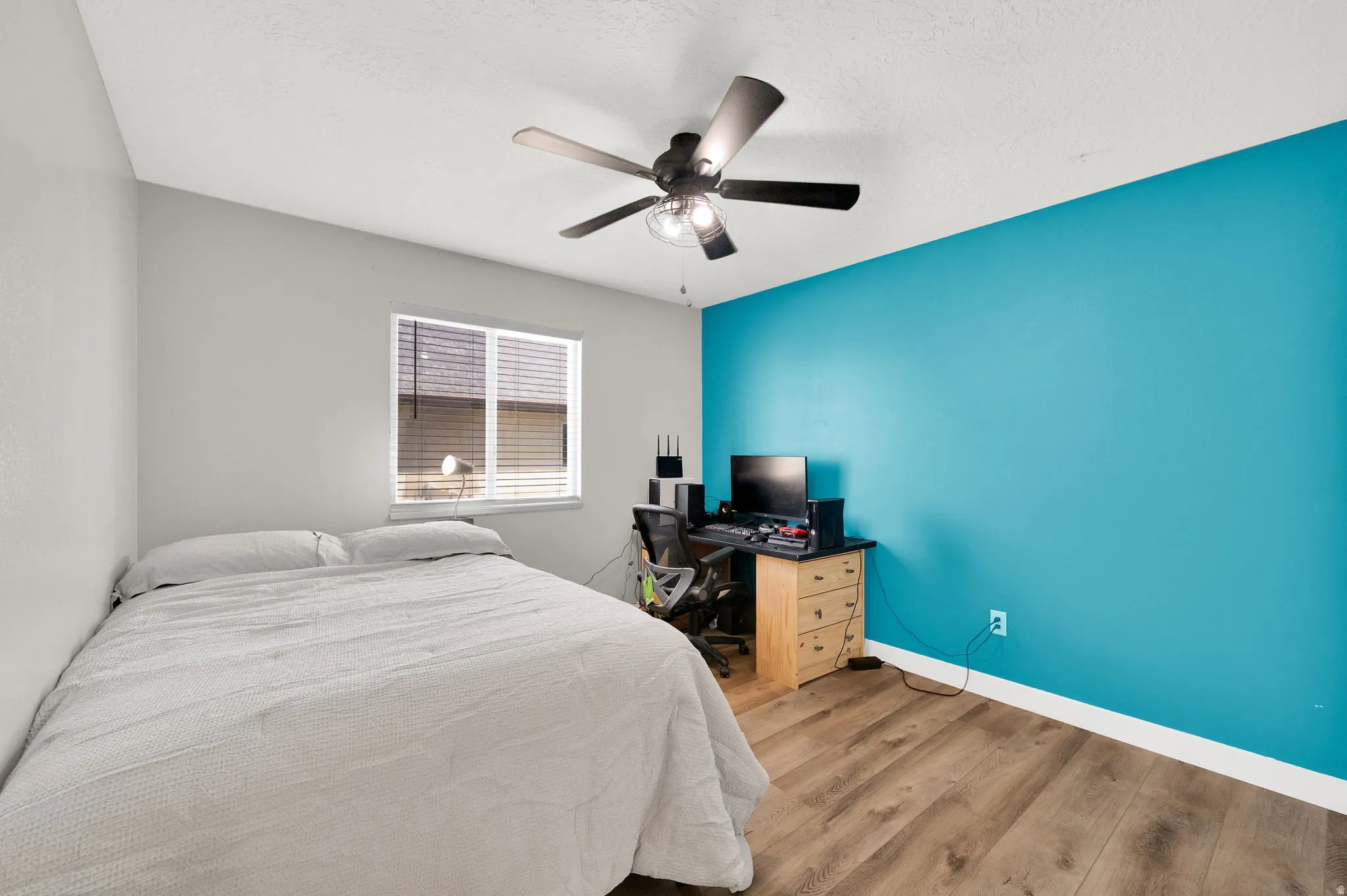 Room featuring a prominent accent wall, wood-finish flooring, and a ceiling fan with integrated lighting