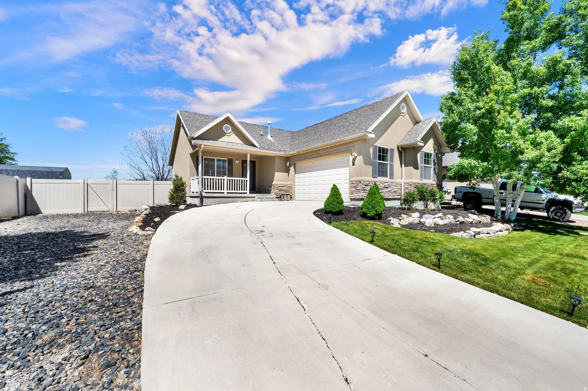 Exterior residence featuring a stucco and stone facade, covered front porch, attached garage, concrete driveway, and a manicured lawn with landscaping