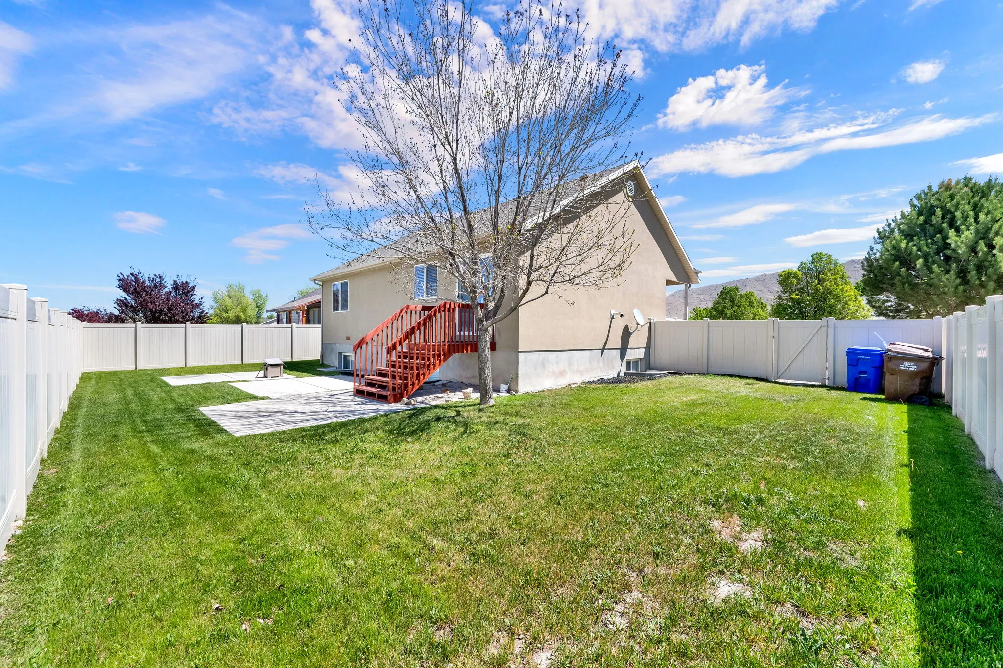 Spacious backyard featuring a manicured lawn, white privacy fencing, and two concrete patio areas