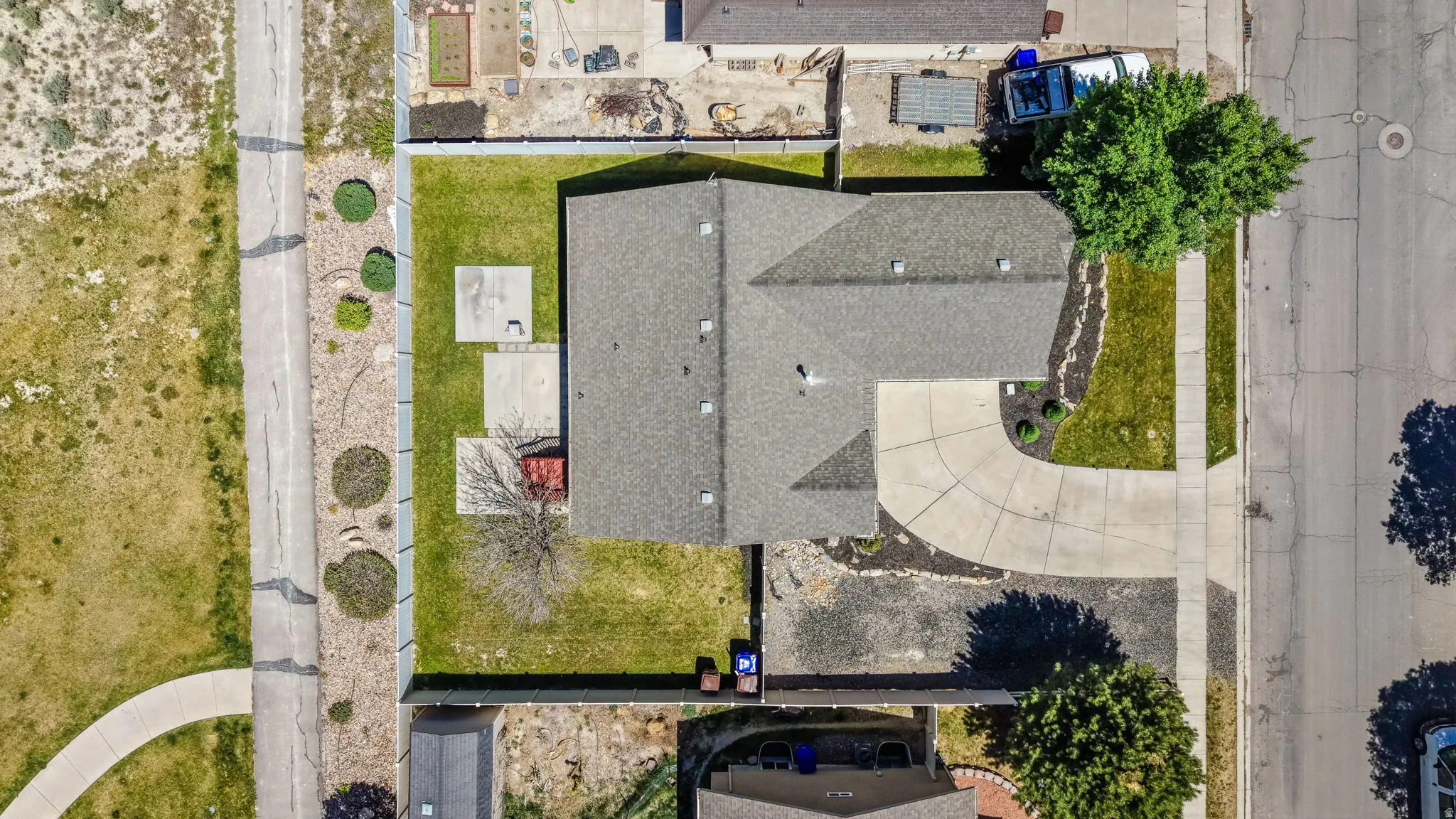 Aerial overview showcasing a single-story residence with a gray shingle roof, green lawn, and concrete driveway