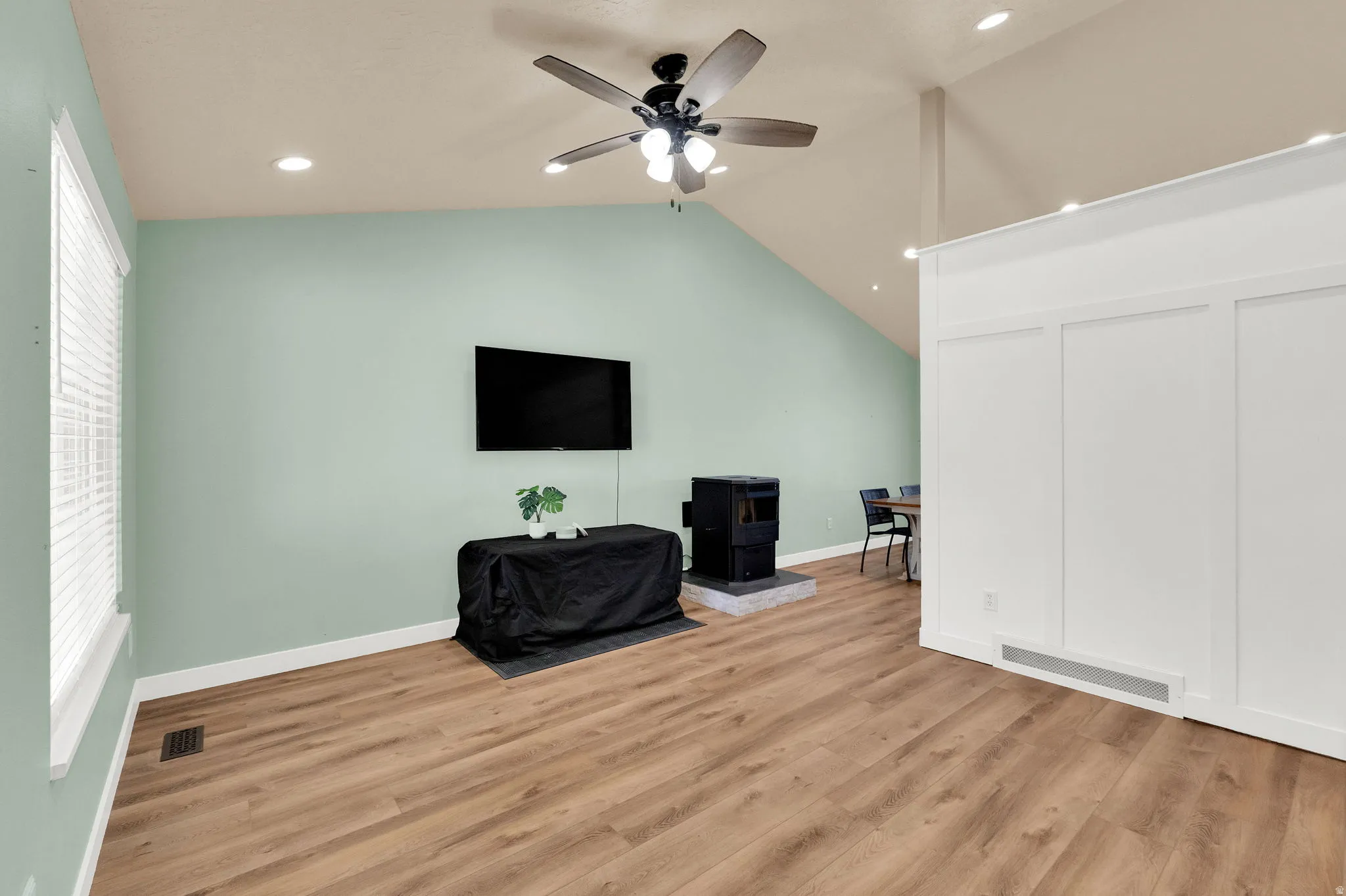 Living space featuring vaulted ceilings, recessed lighting, wood-finish flooring, a contemporary wood stove on a stone hearth, and a board and batten accent wall