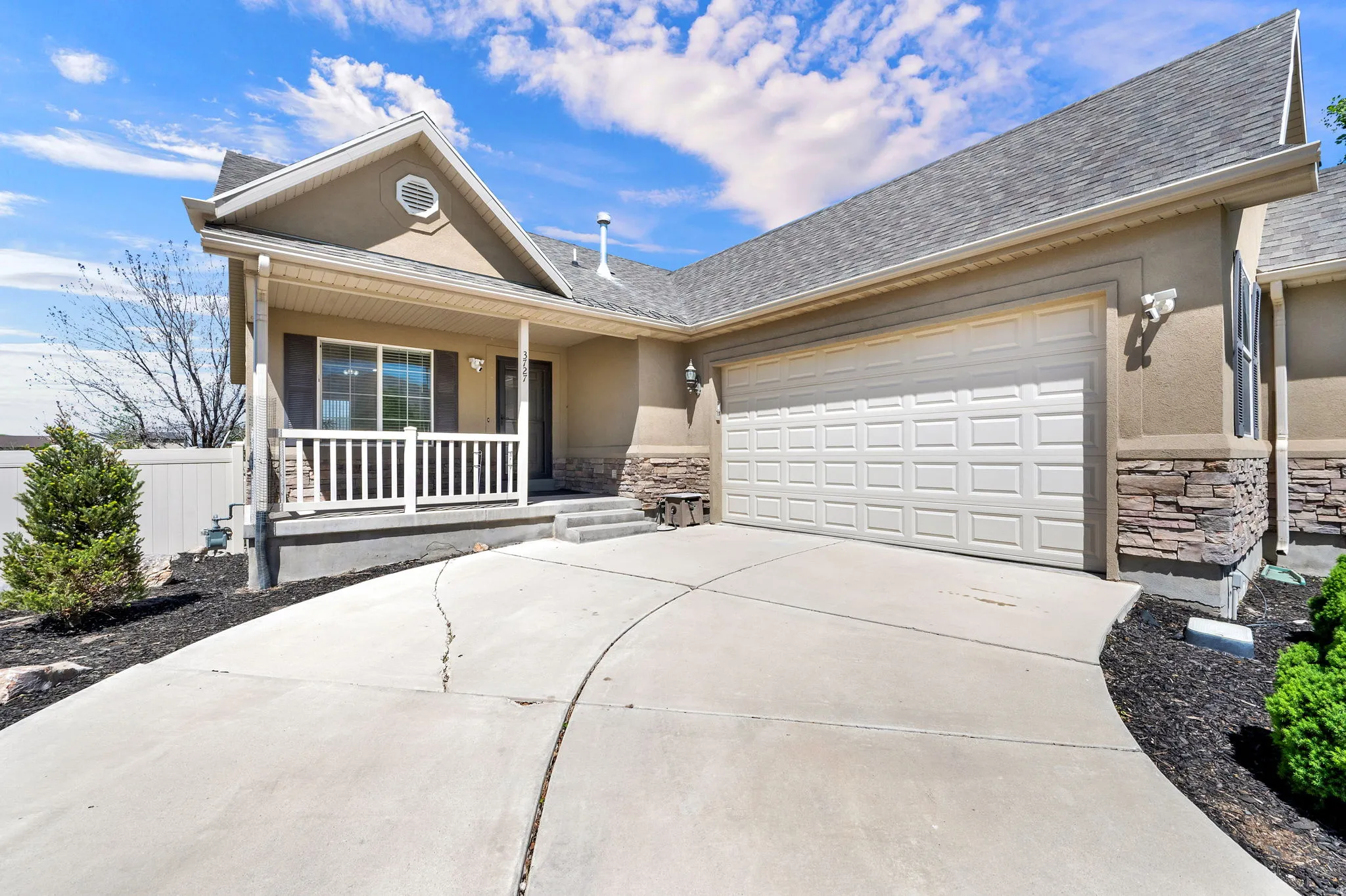 Stucco and stone facade home featuring a two-car garage, covered porch with white railings, and a concrete driveway