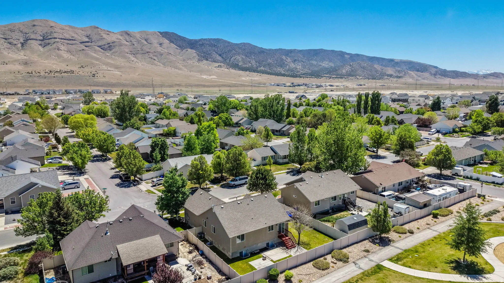 Suburban neighborhood featuring established homes with pitched roofs, mature trees, and mountain backdrop
