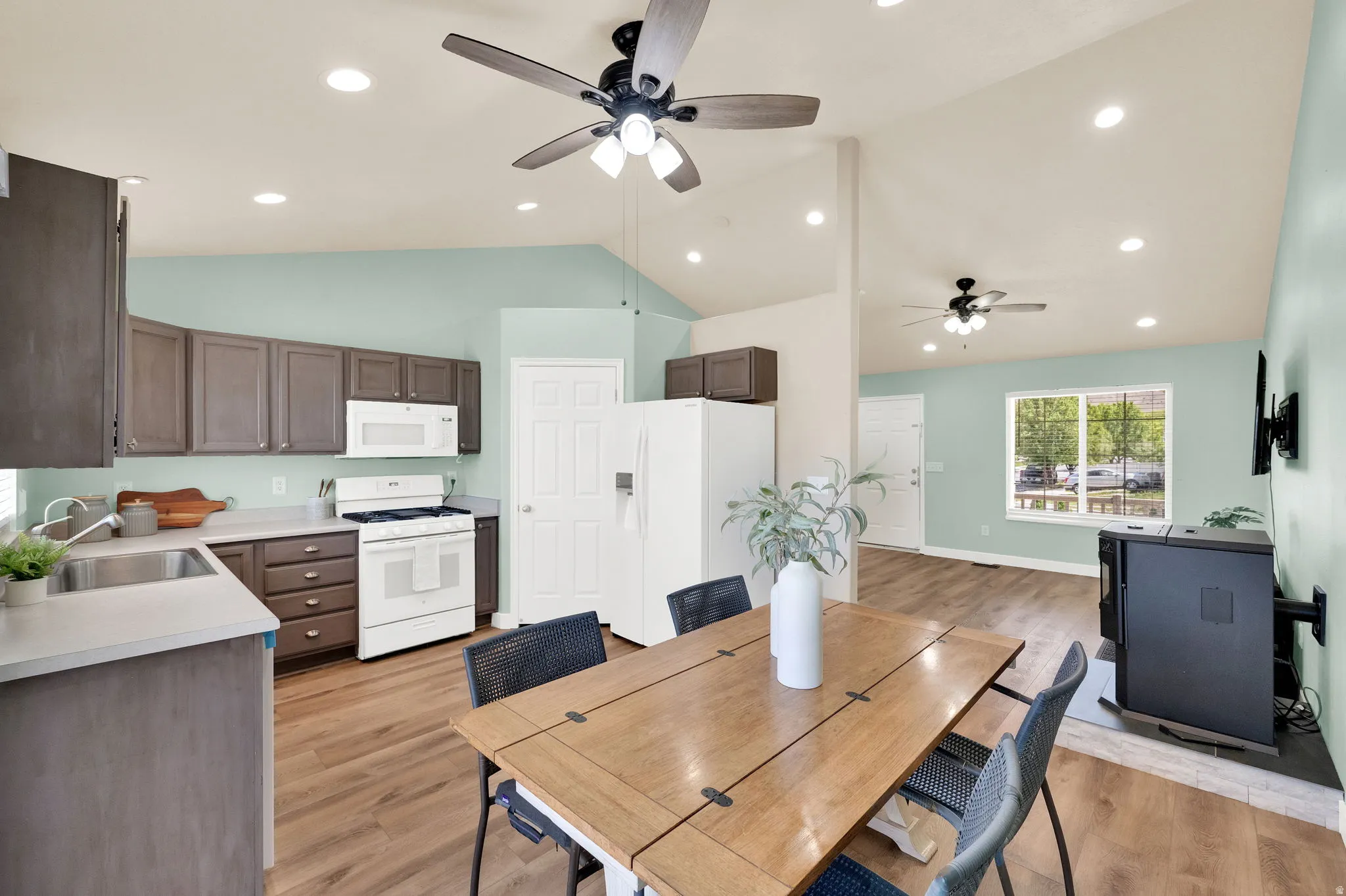 Open-concept kitchen and dining area featuring wood-finish flooring, vaulted ceilings with recessed lighting, and a ceiling fan