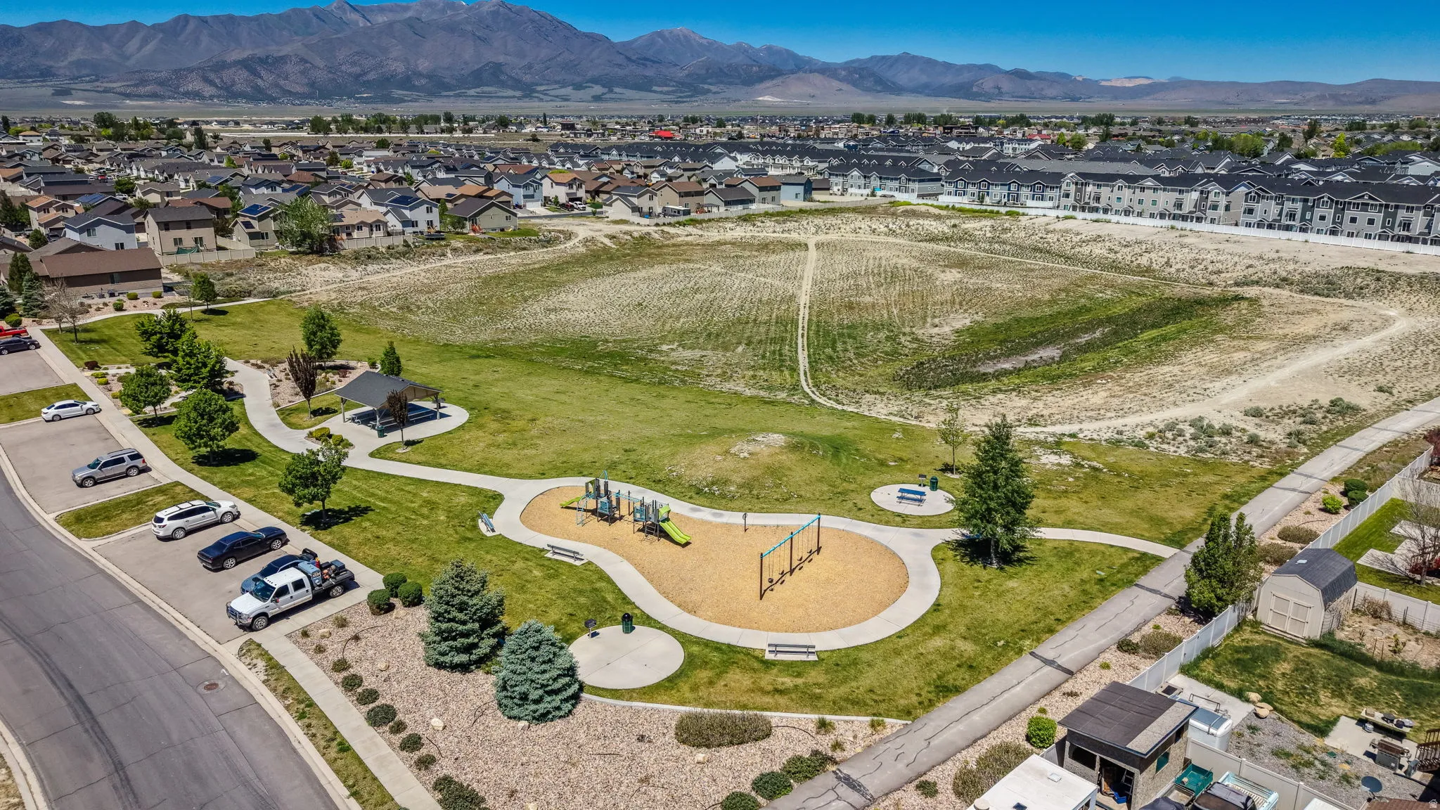 Community park area featuring a playground with wood chip surfacing, a covered picnic shelter, and winding paved pathways