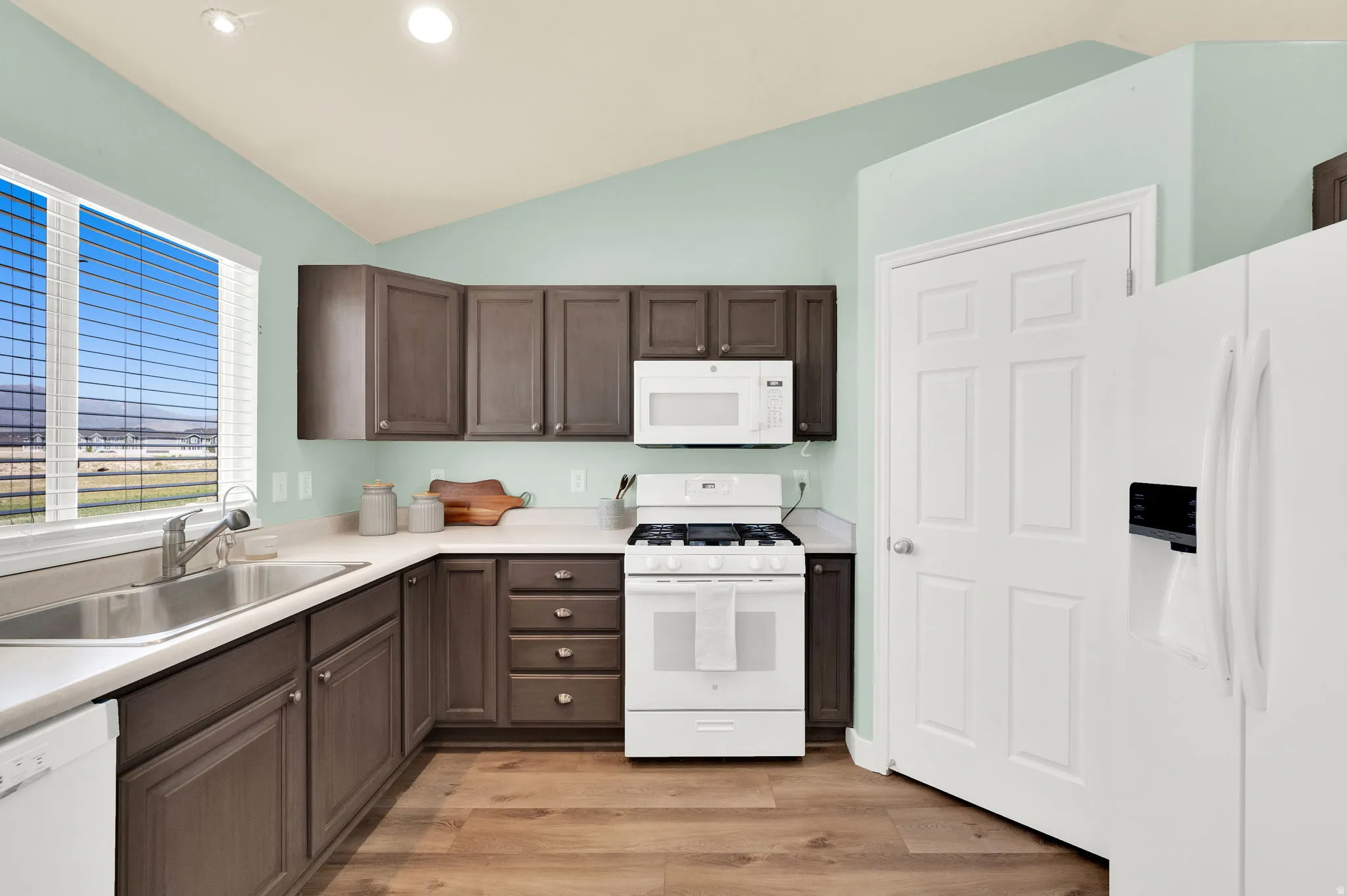 Kitchen featuring wood-finish flooring, dark wood cabinetry, white countertops, and a stainless steel sink