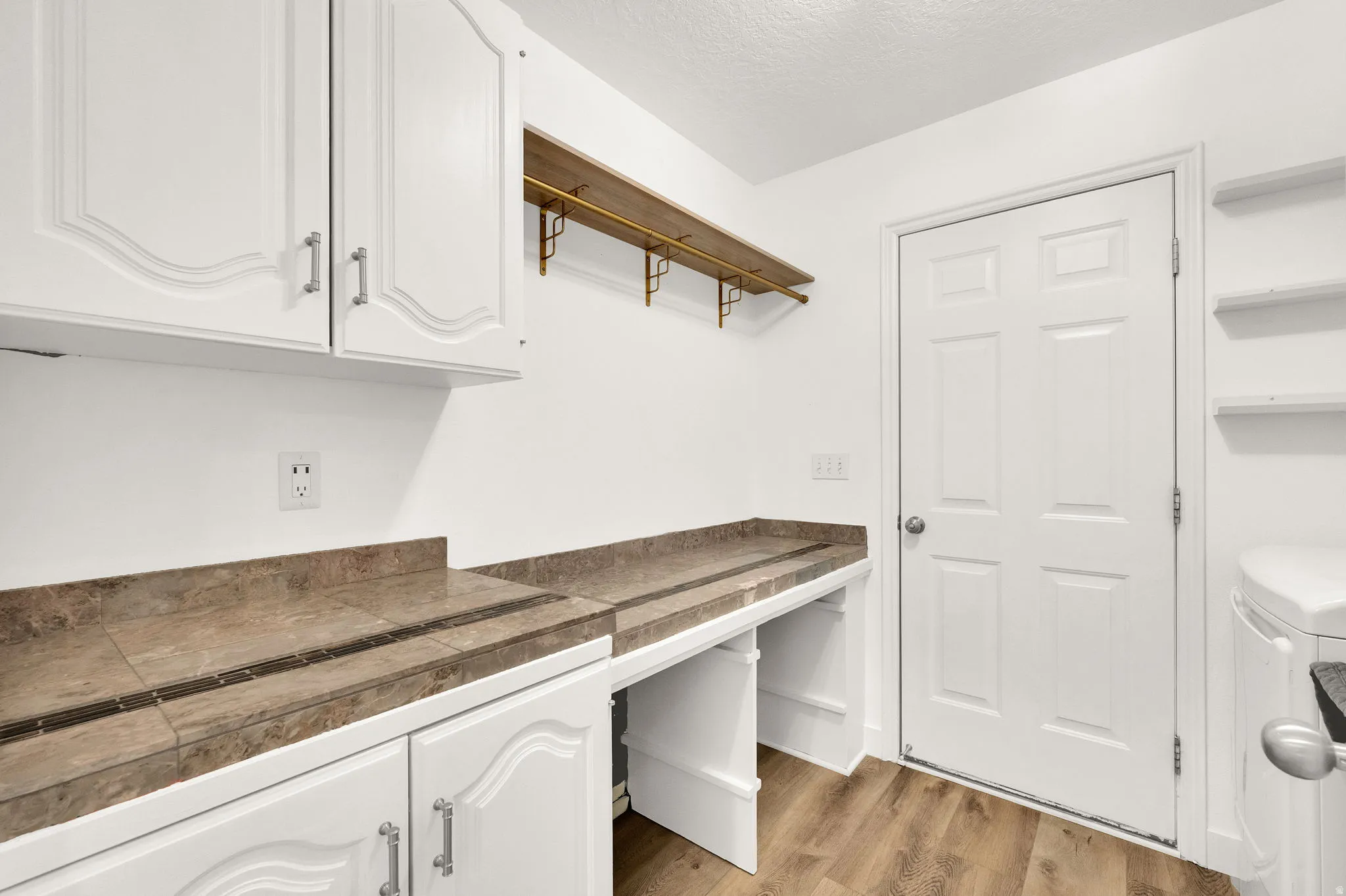 Utility room with wood-finish flooring, white cabinetry, and stone-look countertops