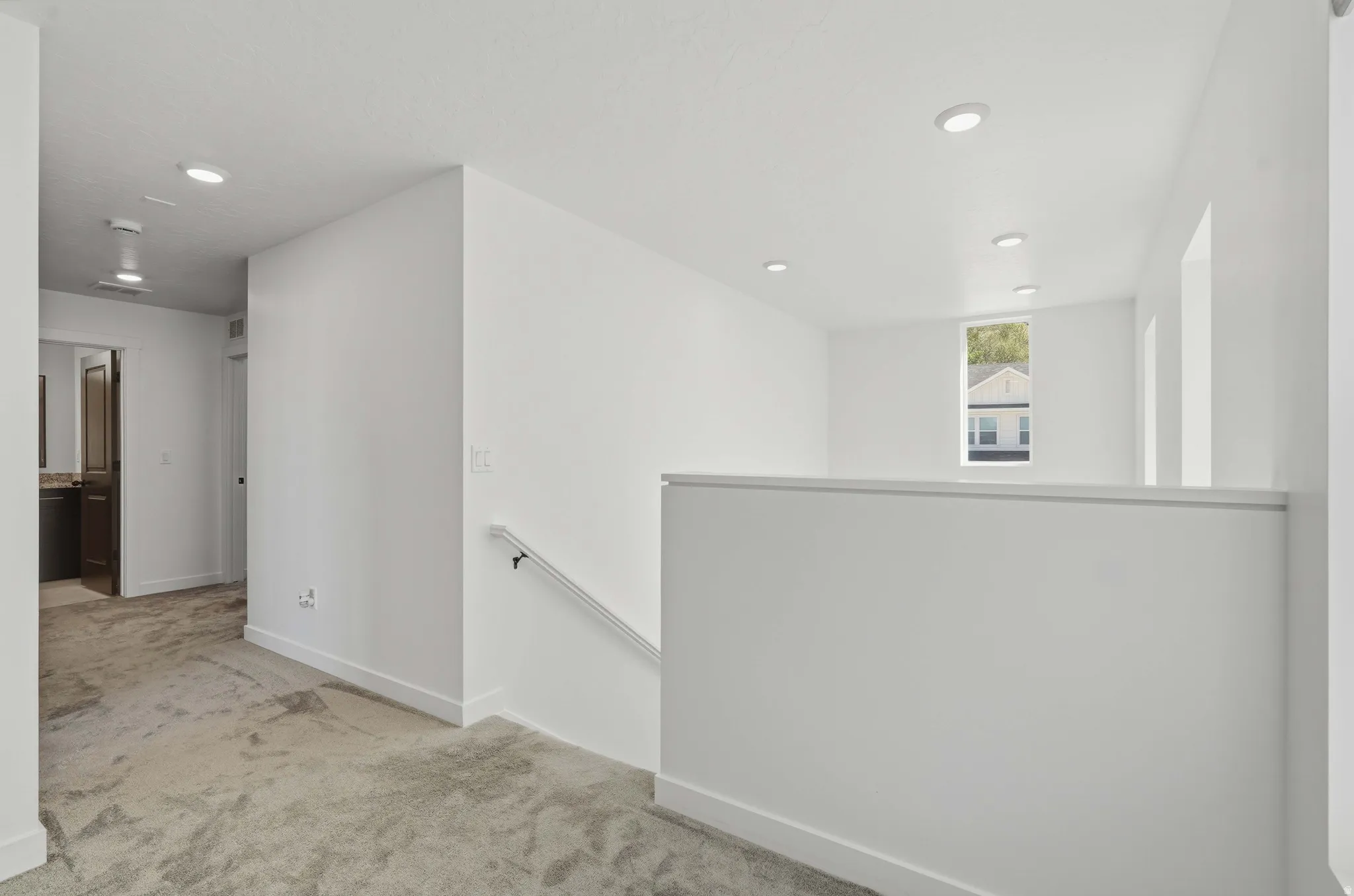 Upper level featuring a carpeted hallway, white walls, recessed lighting, and a window with exterior views